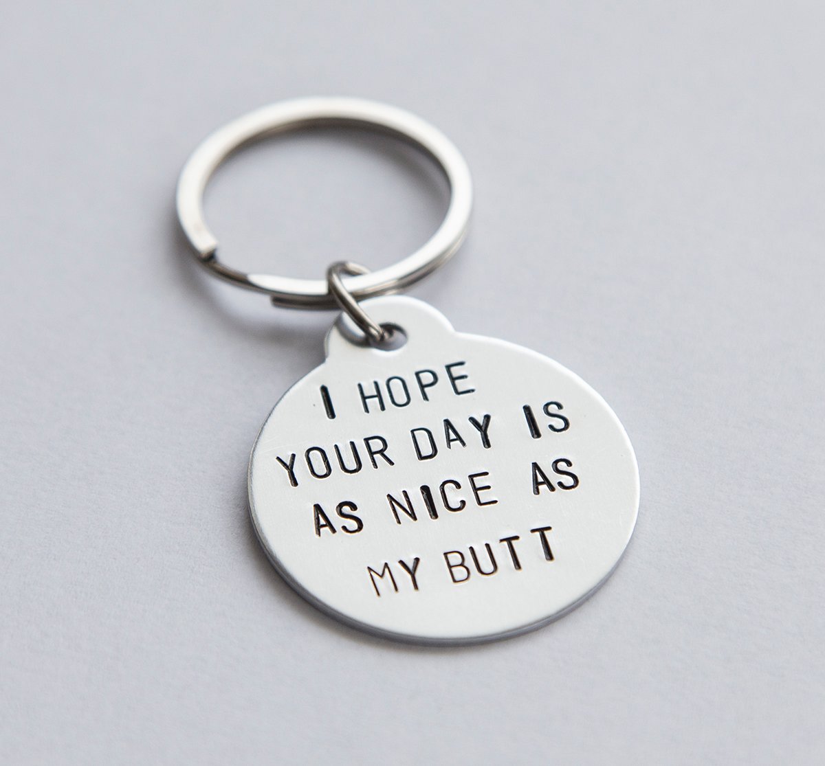 A humorous keyring with the phrase 'I hope your day is as nice as my butt', featuring a stainless steel keyring and lightweight aluminum tag.