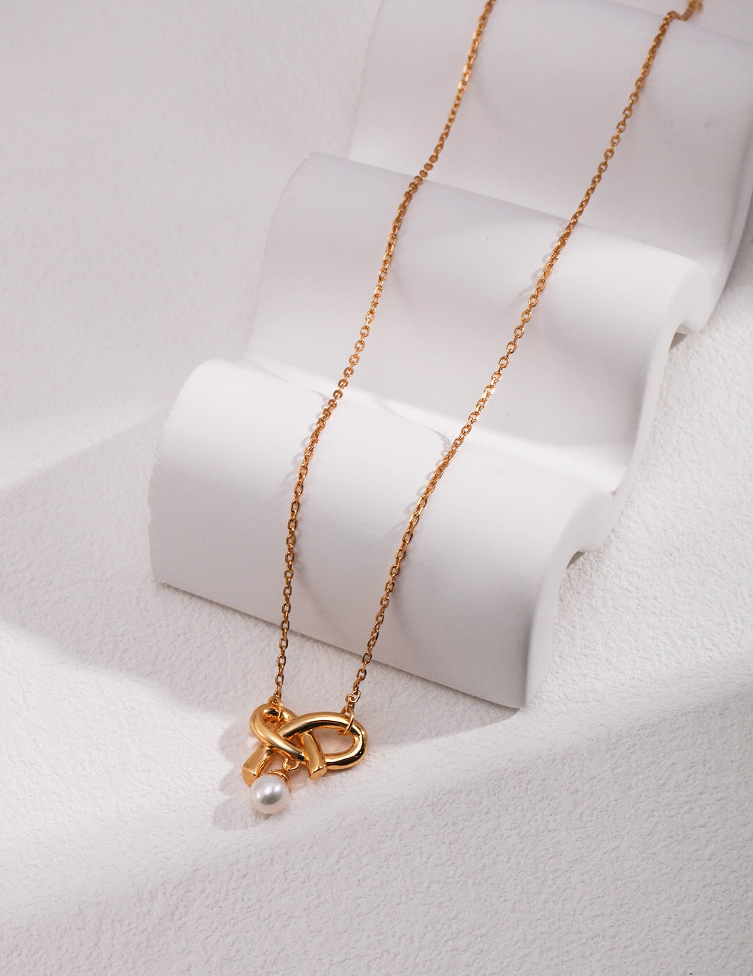 A delicate Love Bow Charm Necklace featuring a floating pearl, elegantly designed with gold vermeil accents.