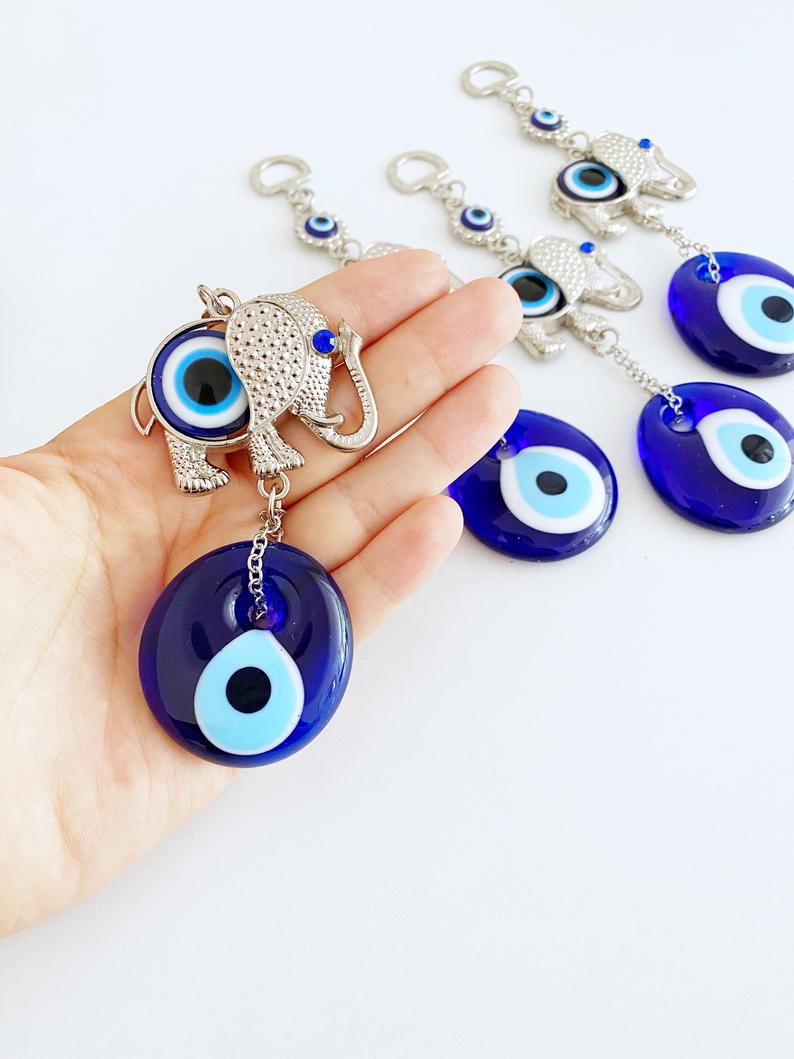 A handmade Lucky Evil Eye Wall Hanging featuring a glass evil eye bead and a silver elephant charm, perfect for home decor.