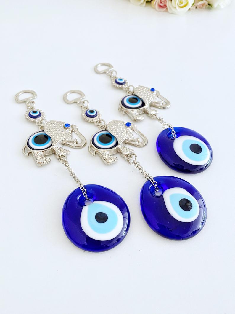 A handmade Lucky Evil Eye Wall Hanging featuring a glass evil eye bead and a silver elephant charm, perfect for home decor.