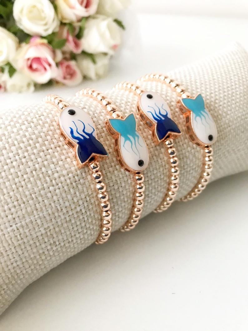 A beautiful rose gold beaded bracelet featuring a fish charm and an evil eye symbol, showcasing elegance and protection.