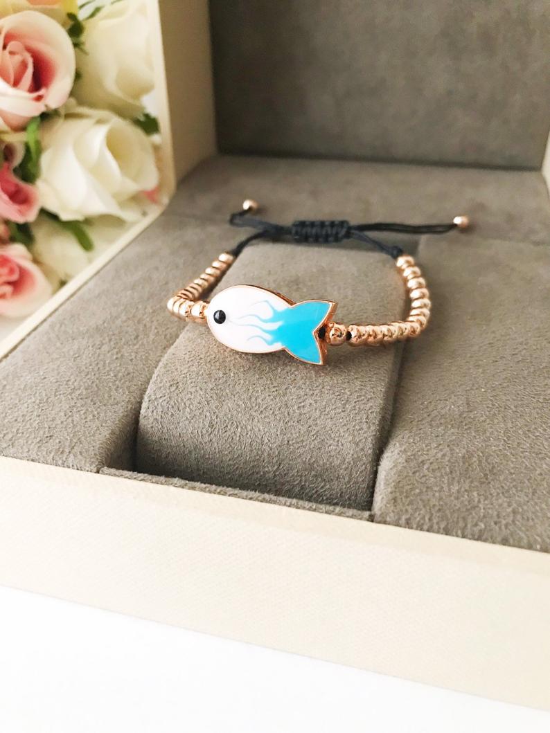 A beautiful rose gold beaded bracelet featuring a fish charm and an evil eye symbol, showcasing elegance and protection.