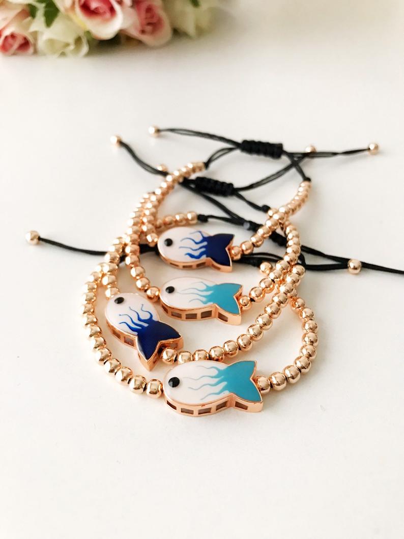 A beautiful rose gold beaded bracelet featuring a fish charm and an evil eye symbol, showcasing elegance and protection.