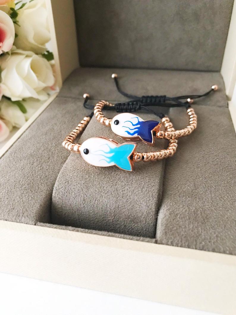 A beautiful rose gold beaded bracelet featuring a fish charm and an evil eye symbol, showcasing elegance and protection.