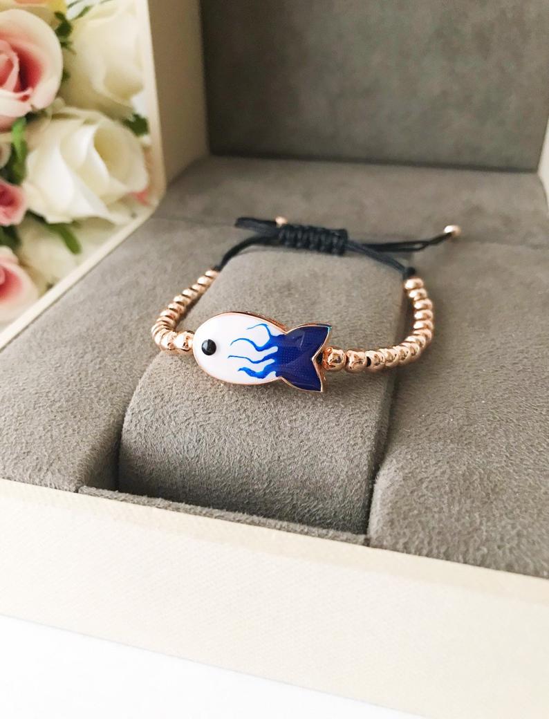 A beautiful rose gold beaded bracelet featuring a fish charm and an evil eye symbol, showcasing elegance and protection.
