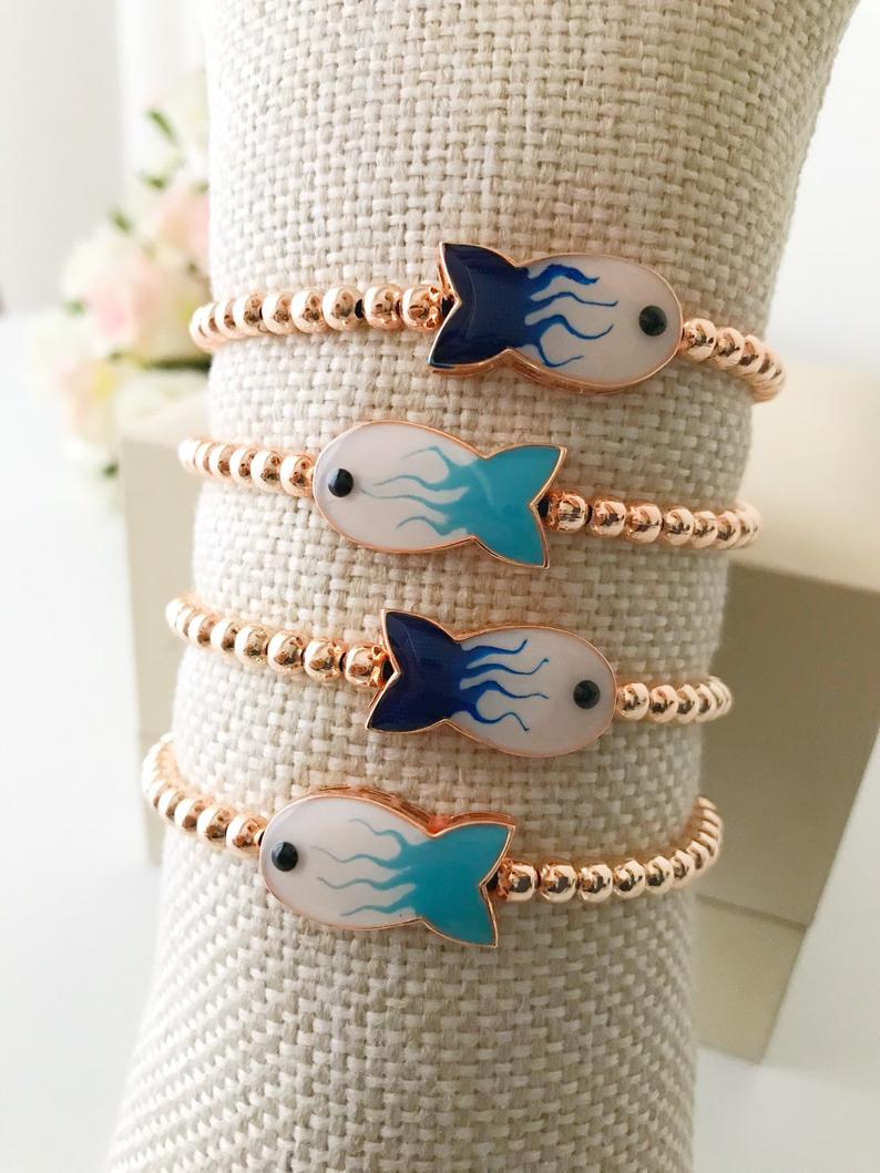 A beautiful rose gold beaded bracelet featuring a fish charm and an evil eye symbol, showcasing elegance and protection.