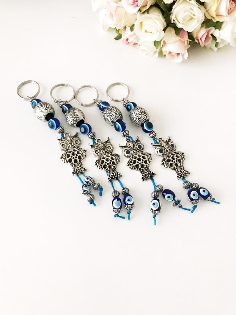 A detailed metal owl keychain featuring a blue evil eye bead, symbolizing protection and luck.