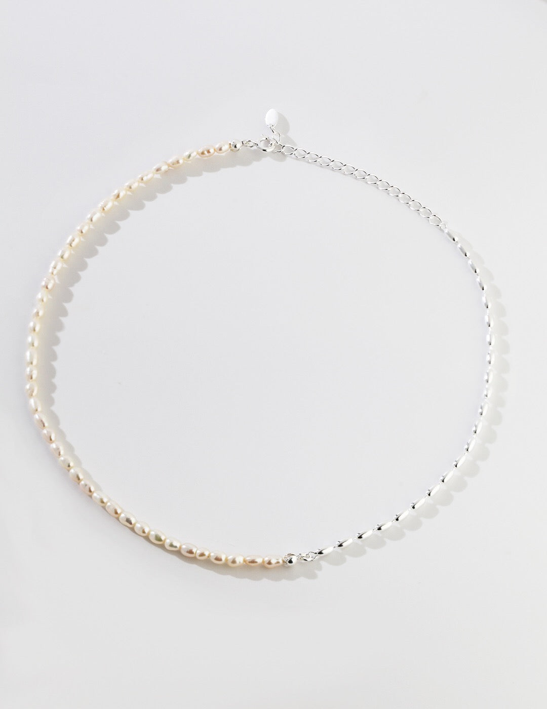 A delicate Minimalist Rice Bead Chain Asymmetric Necklace featuring natural pearls and sterling silver, elegantly displayed on a soft background.