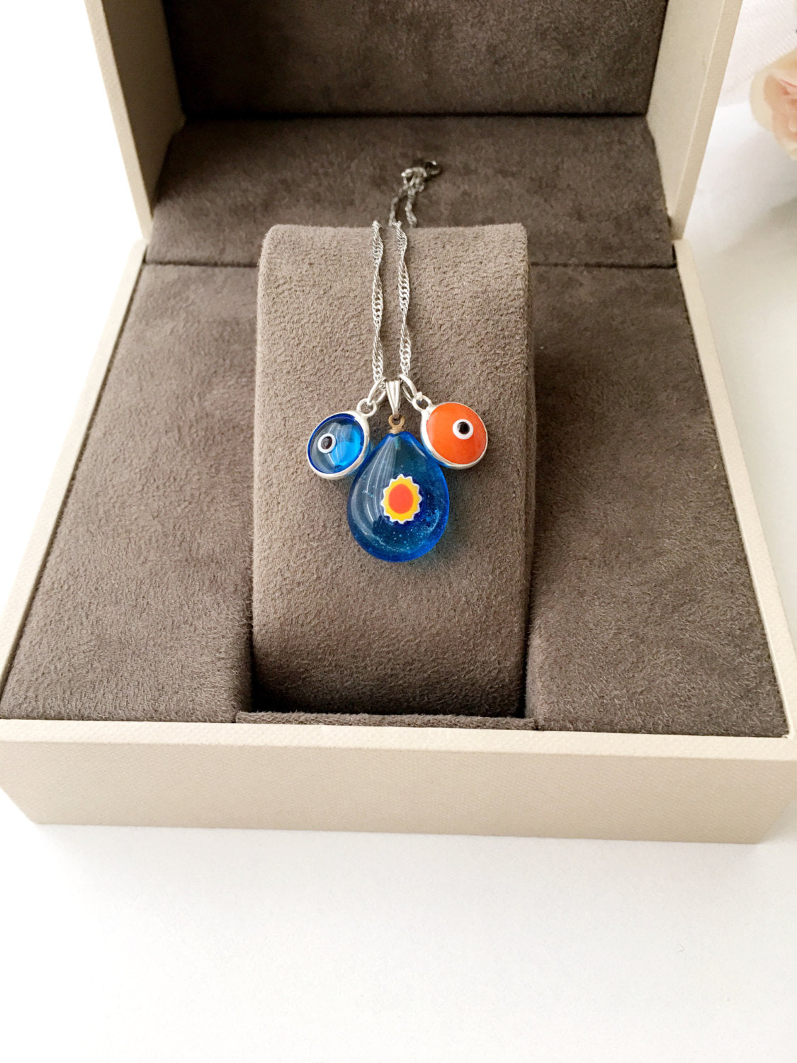 A beautifully handcrafted Murano glass evil eye necklace featuring a large central evil eye bead and smaller orange and turquoise beads.