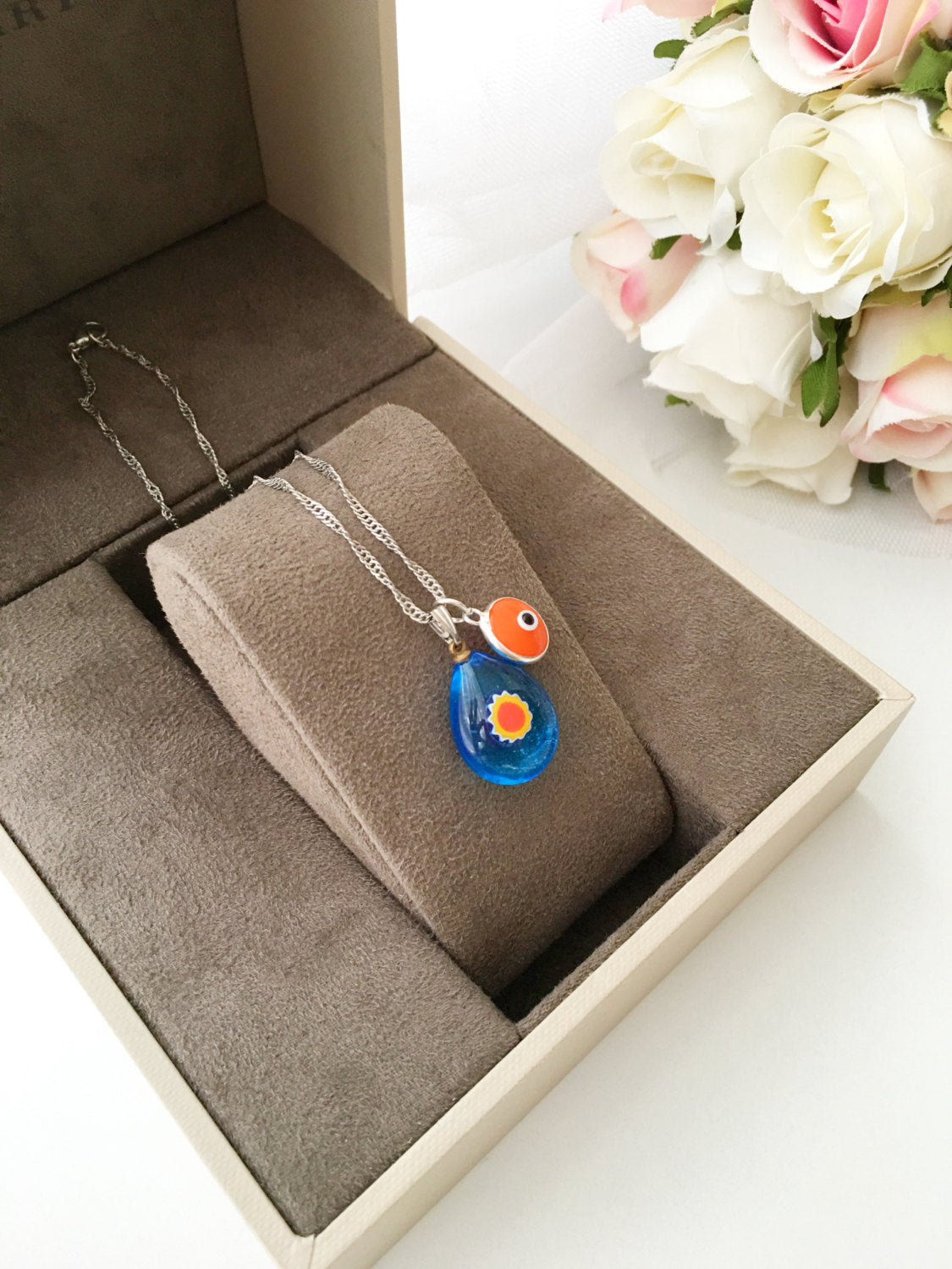 A beautifully handcrafted Murano glass evil eye necklace featuring a large central evil eye bead and smaller orange and turquoise beads.