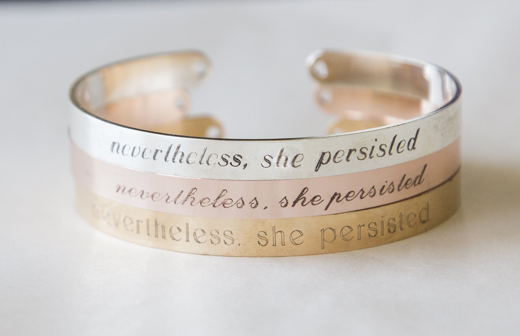 A beautifully crafted 'Nevertheless She Persisted' bracelet, featuring an adjustable cuff design in silver and gold plating, showcasing an empowering engraved message.