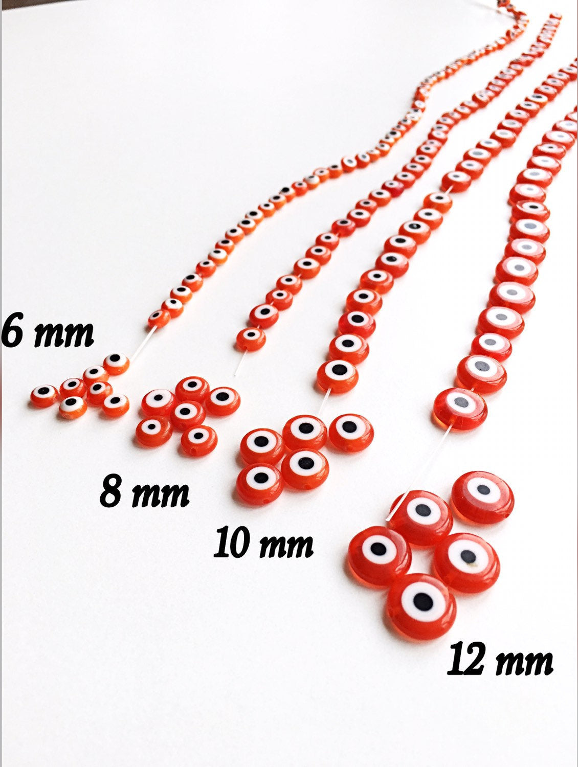 A collection of vibrant orange evil eye beads in various sizes, showcasing their unique handmade designs.