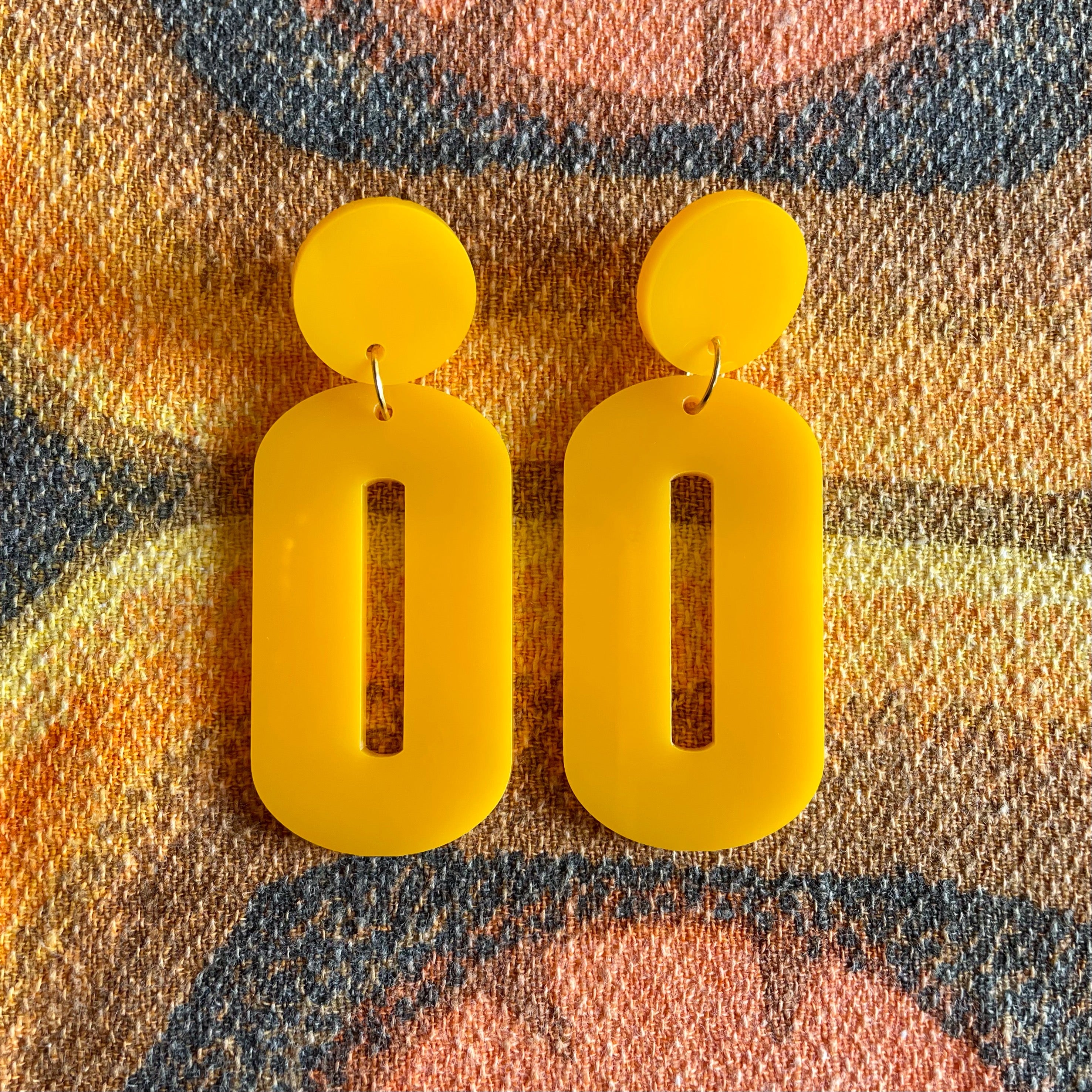 A pair of stylish oval drop earrings made from laser-cut acrylic, showcasing their elegant design and available colors.