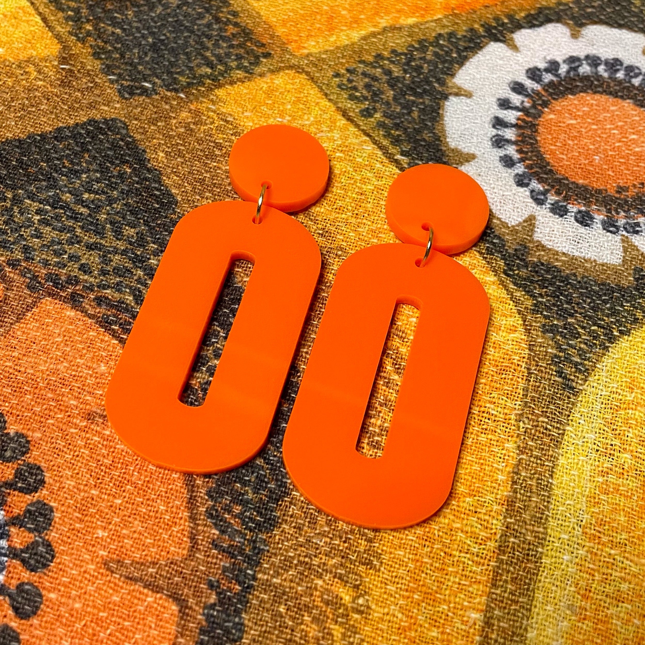 A pair of stylish oval drop earrings made from laser-cut acrylic, showcasing their elegant design and available colors.