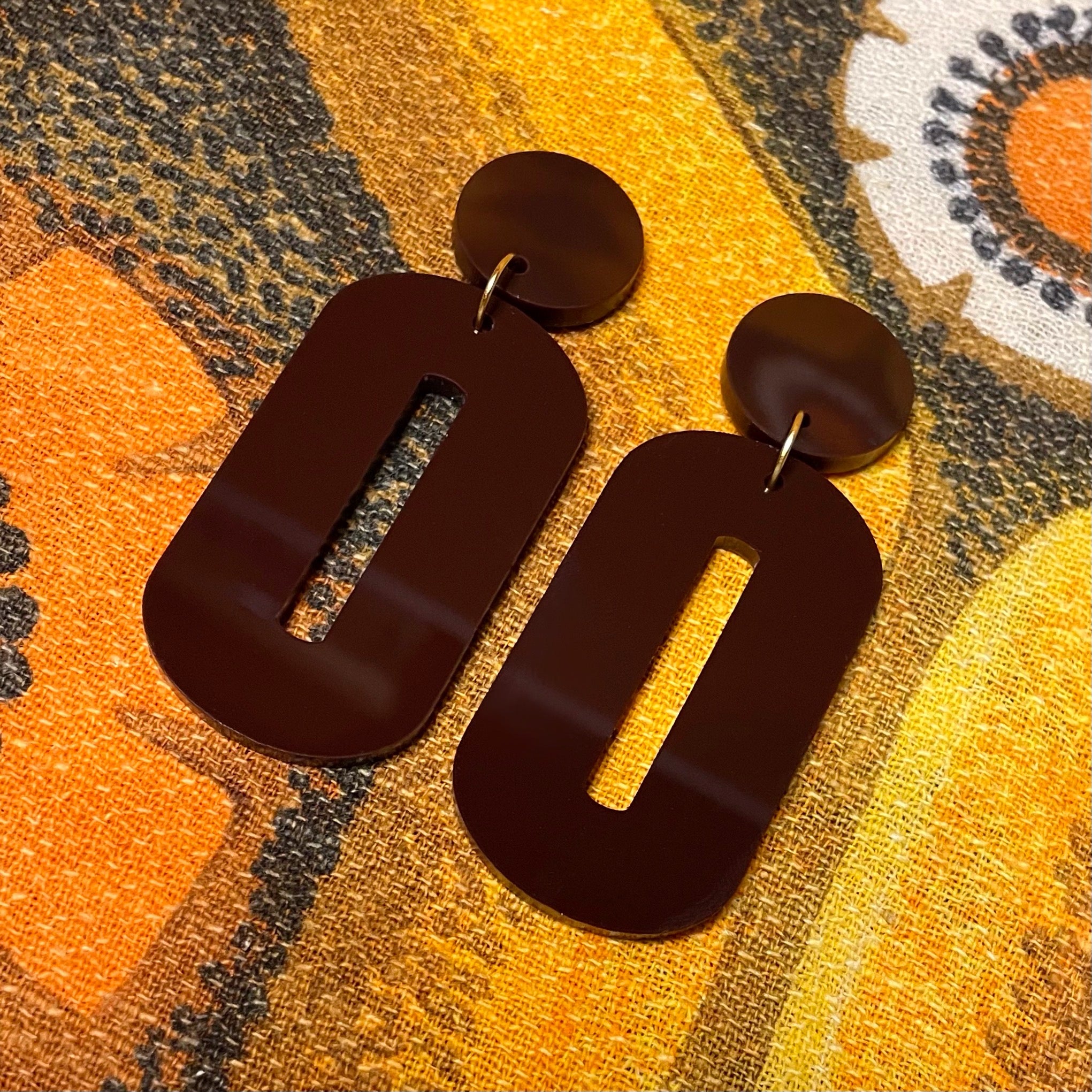 A pair of stylish oval drop earrings made from laser-cut acrylic, showcasing their elegant design and available colors.