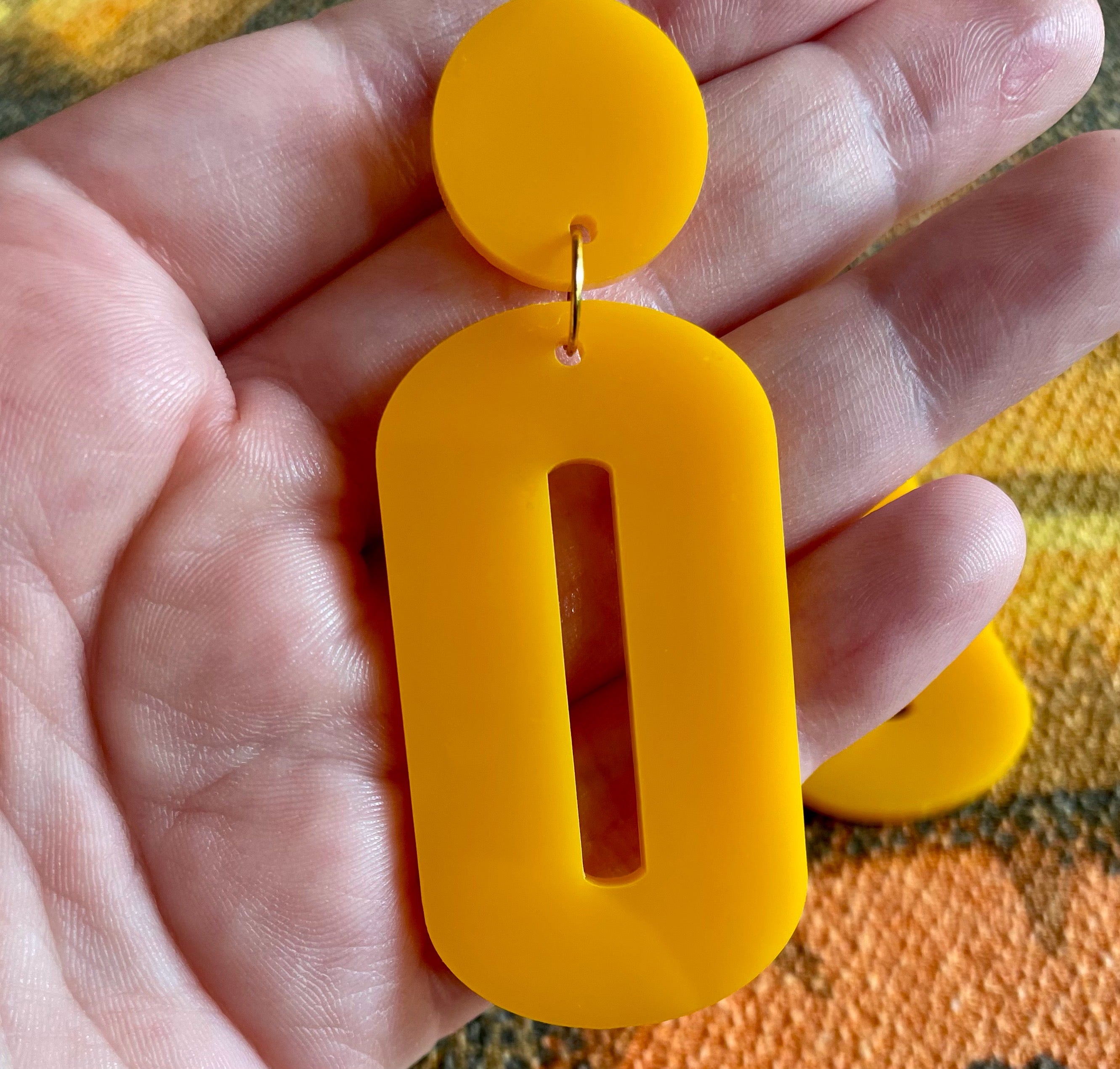 A pair of stylish oval drop earrings made from laser-cut acrylic, showcasing their elegant design and available colors.