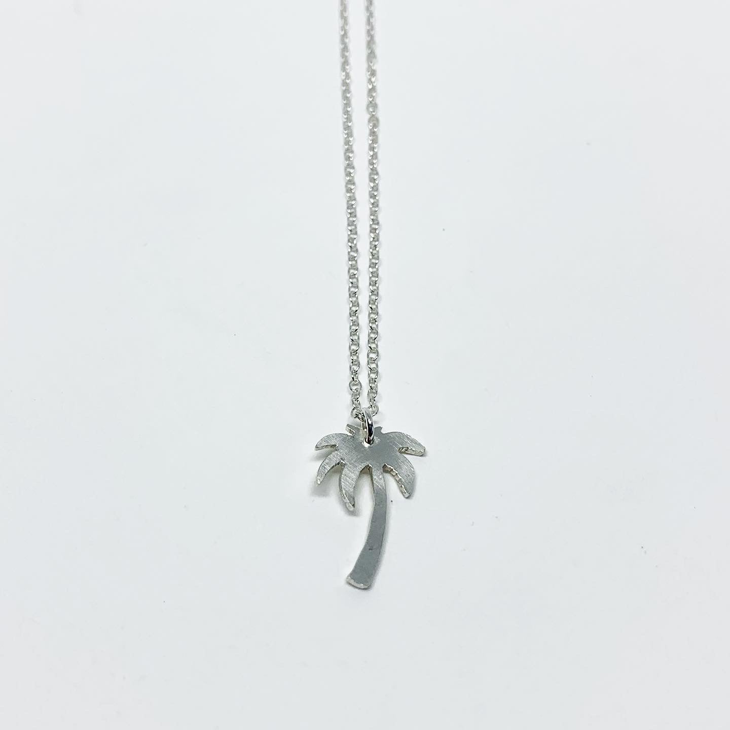 A delicate Palm Tree Charm Necklace featuring a hand-cut palm tree pendant in recycled sterling silver, displayed on a lightweight adjustable chain.