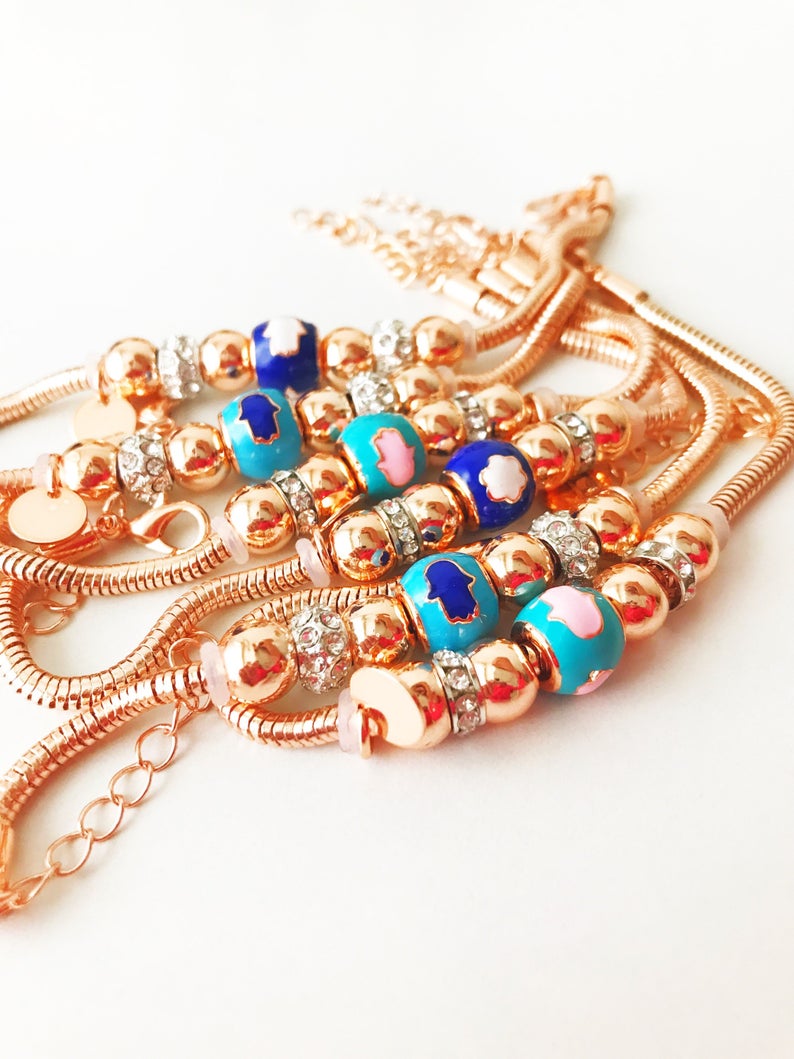 A beautiful rose gold Pandora charm bracelet featuring various charms including a hamsa hand, four-leaf clover, and star, made from tarnish-resistant stainless steel.