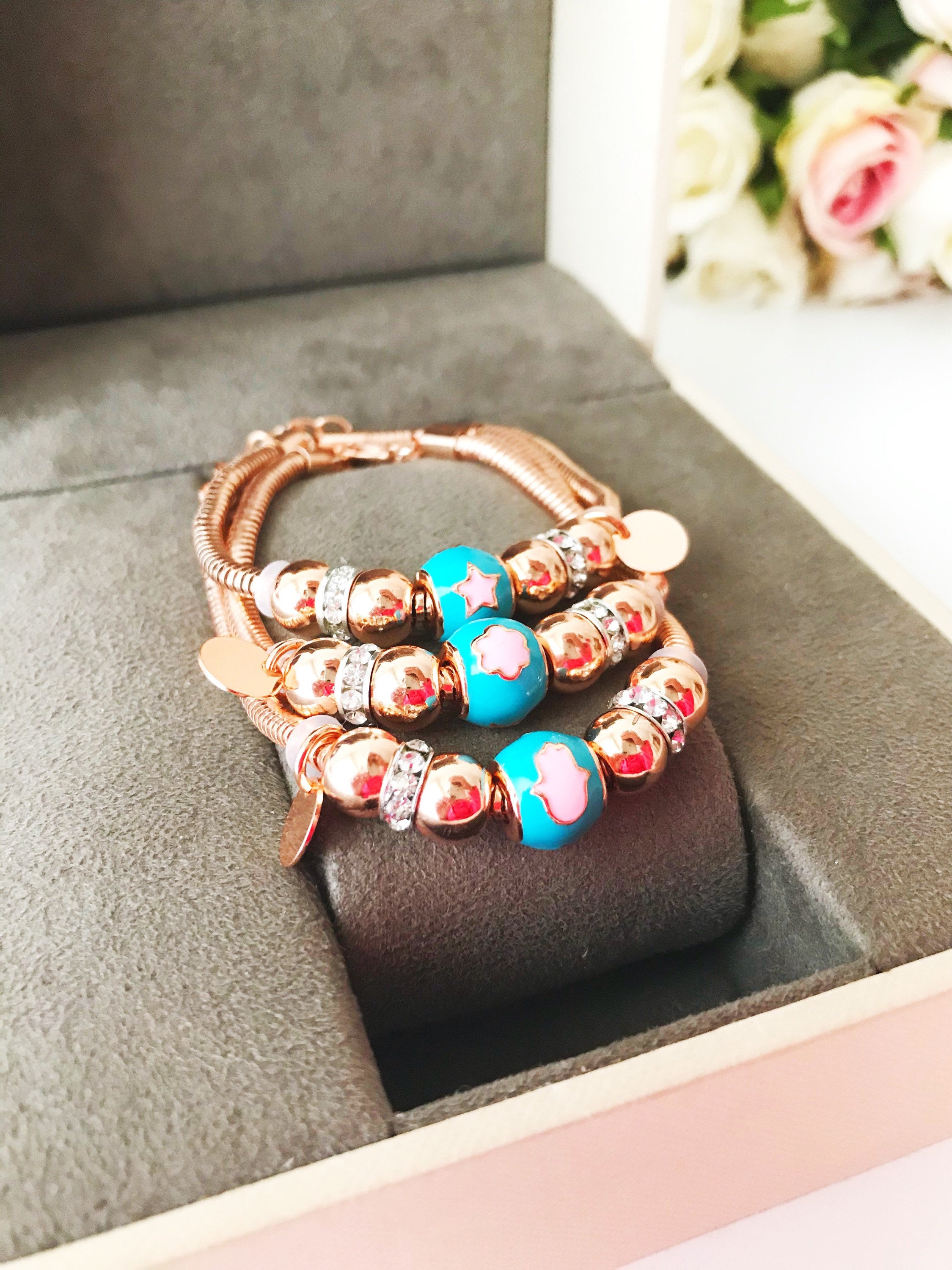 A beautiful rose gold Pandora charm bracelet featuring various charms including a hamsa hand, four-leaf clover, and star, made from tarnish-resistant stainless steel.