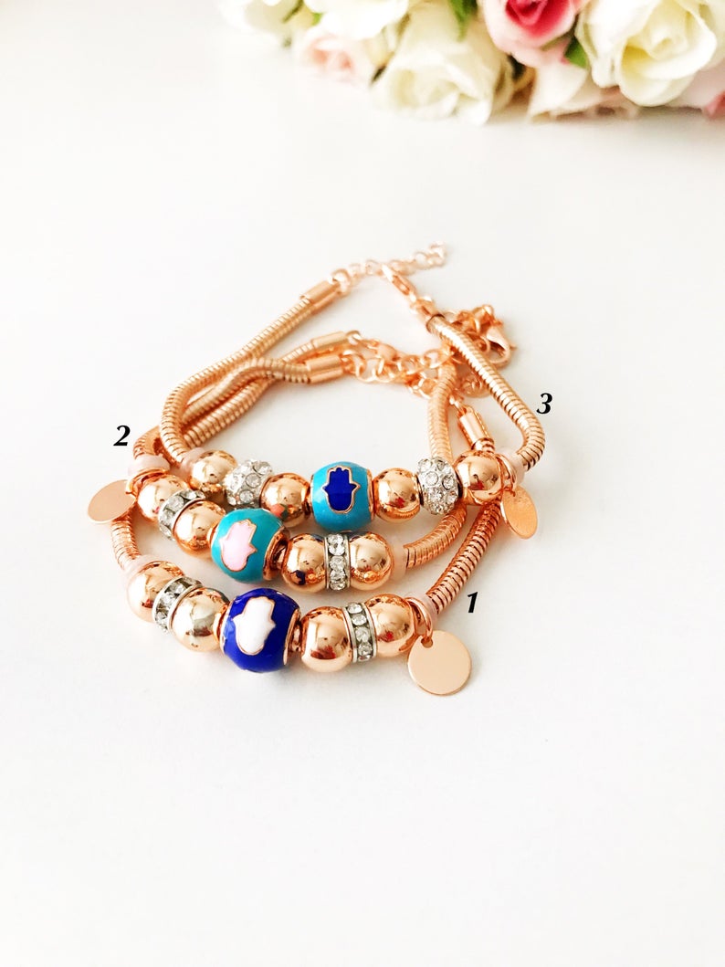 A beautiful rose gold Pandora charm bracelet featuring various charms including a hamsa hand, four-leaf clover, and star, made from tarnish-resistant stainless steel.