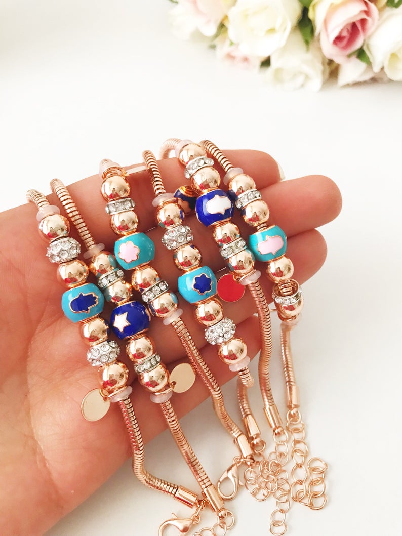 A beautiful rose gold Pandora charm bracelet featuring various charms including a hamsa hand, four-leaf clover, and star, made from tarnish-resistant stainless steel.