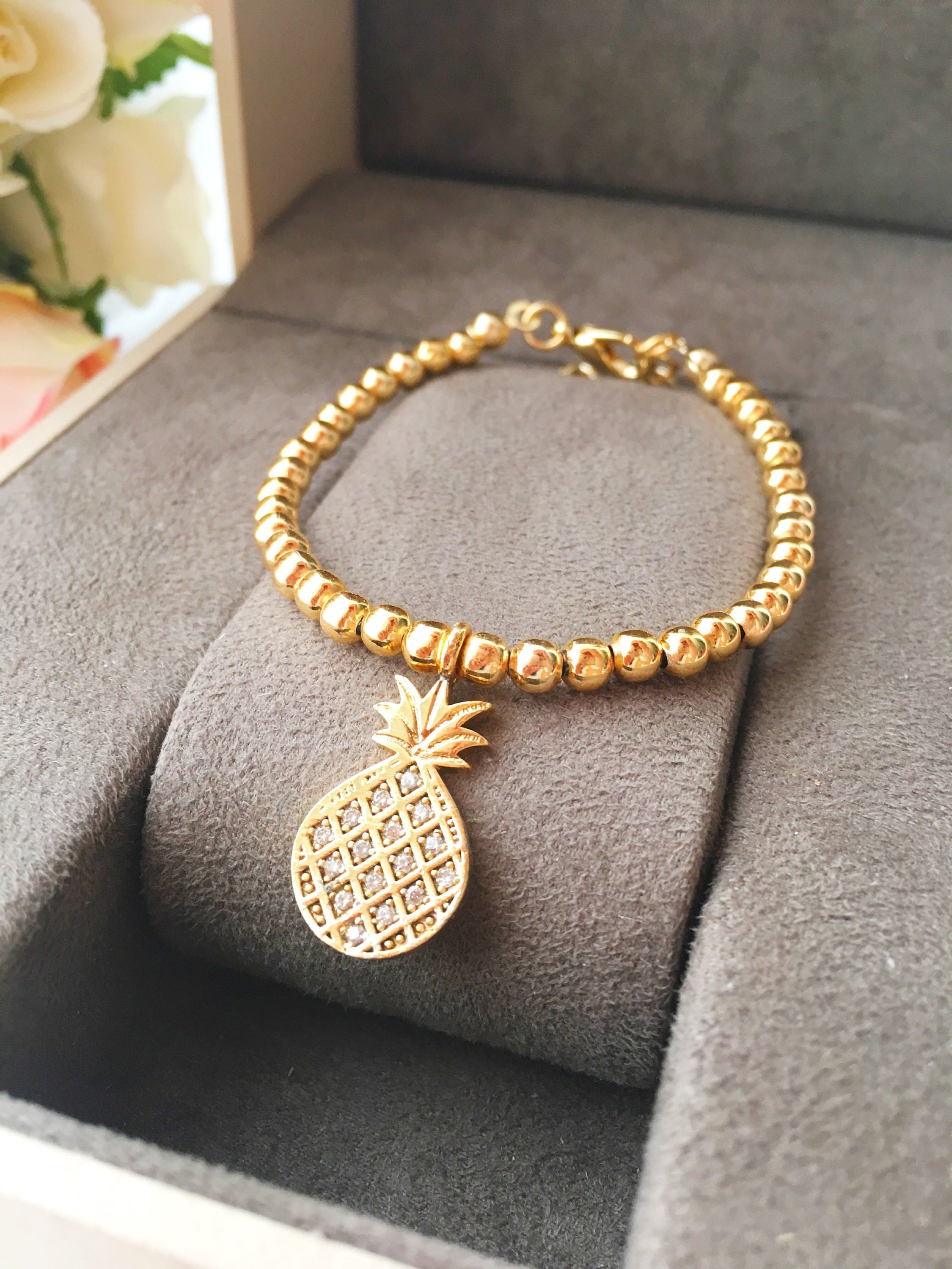A delicate gold beaded bracelet featuring a pineapple charm, showcasing its adjustable design and handmade craftsmanship.