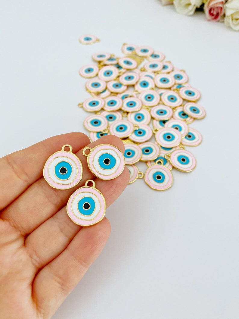 A beautiful pink evil eye charm with gold plating, featuring a traditional evil eye design, perfect for jewelry making.