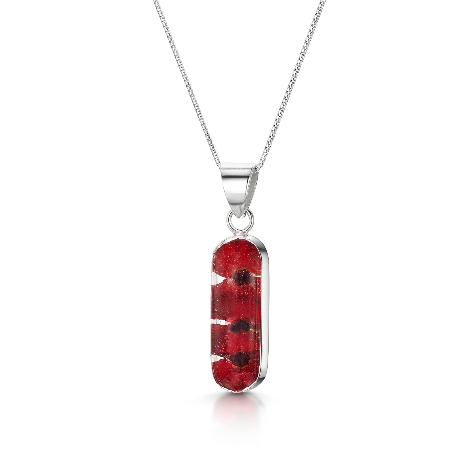 Poppy necklace 'Leela' featuring a vertical bar pendant with tiny red Euphorbia Milii flowers encased in resin, on a sterling silver chain.