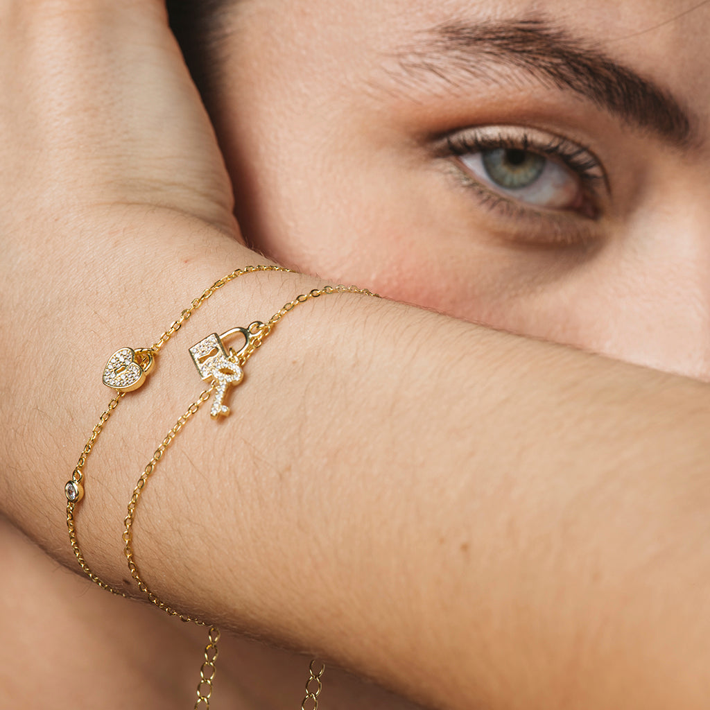 Pulsera elegante bañada en oro amarillo con circonitas blancas, motivos de llave y candado, ajustable y con cierre seguro.