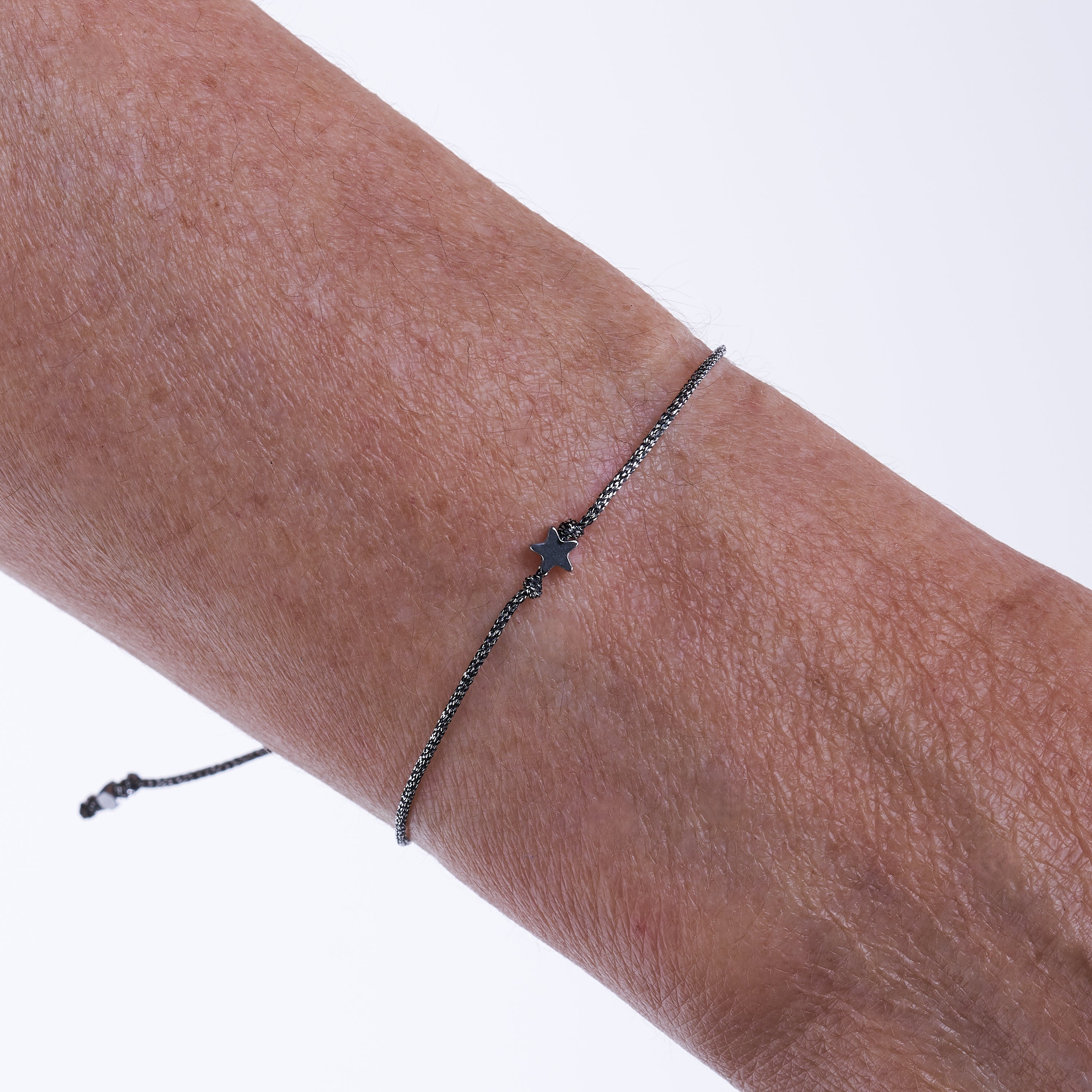 Pulsera con estrella diminuta de hematita sobre fondo blanco, mostrando su diseño delicado y cordón metálico gris oscuro.