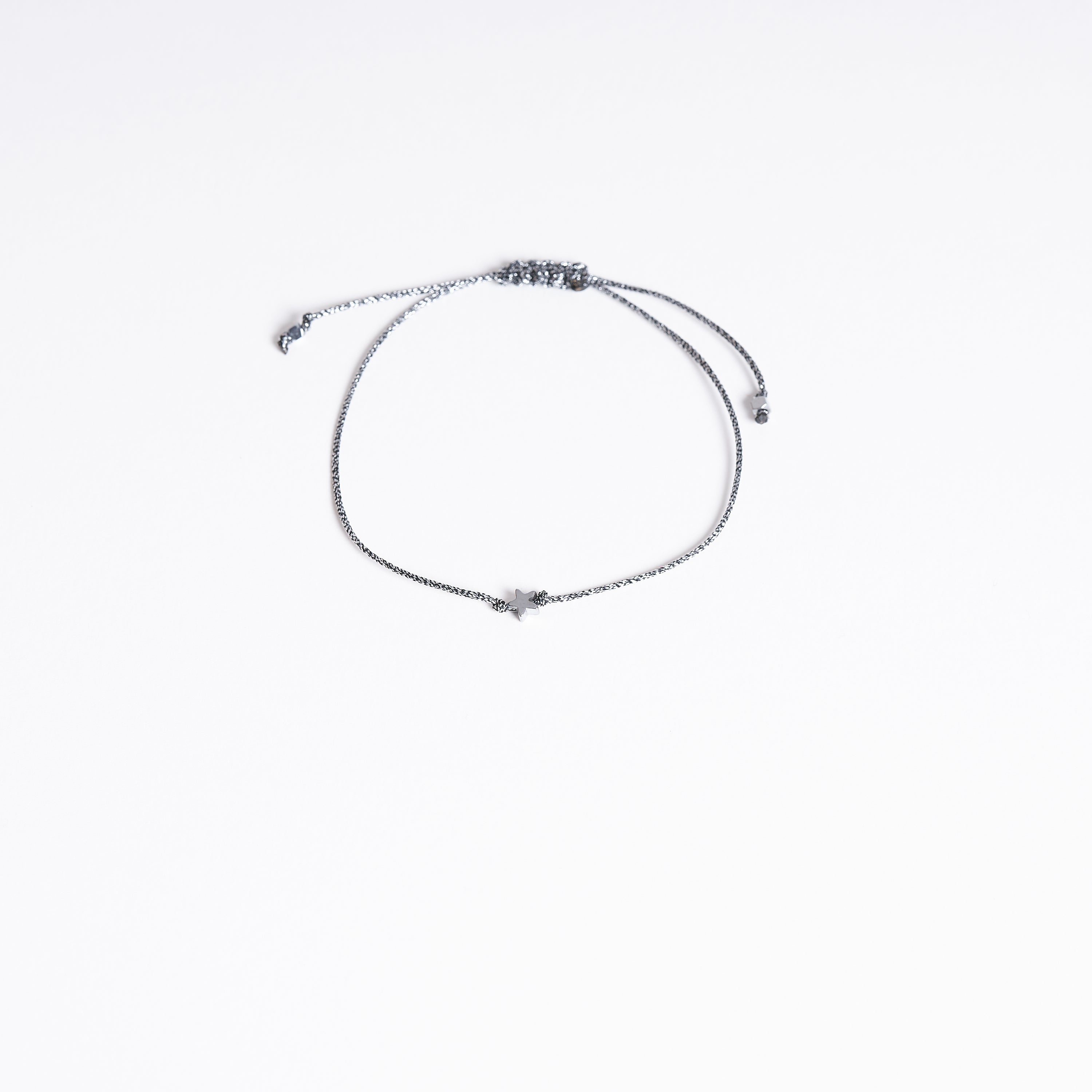 Pulsera con estrella diminuta de hematita sobre fondo blanco, mostrando su diseño delicado y cordón metálico gris oscuro.