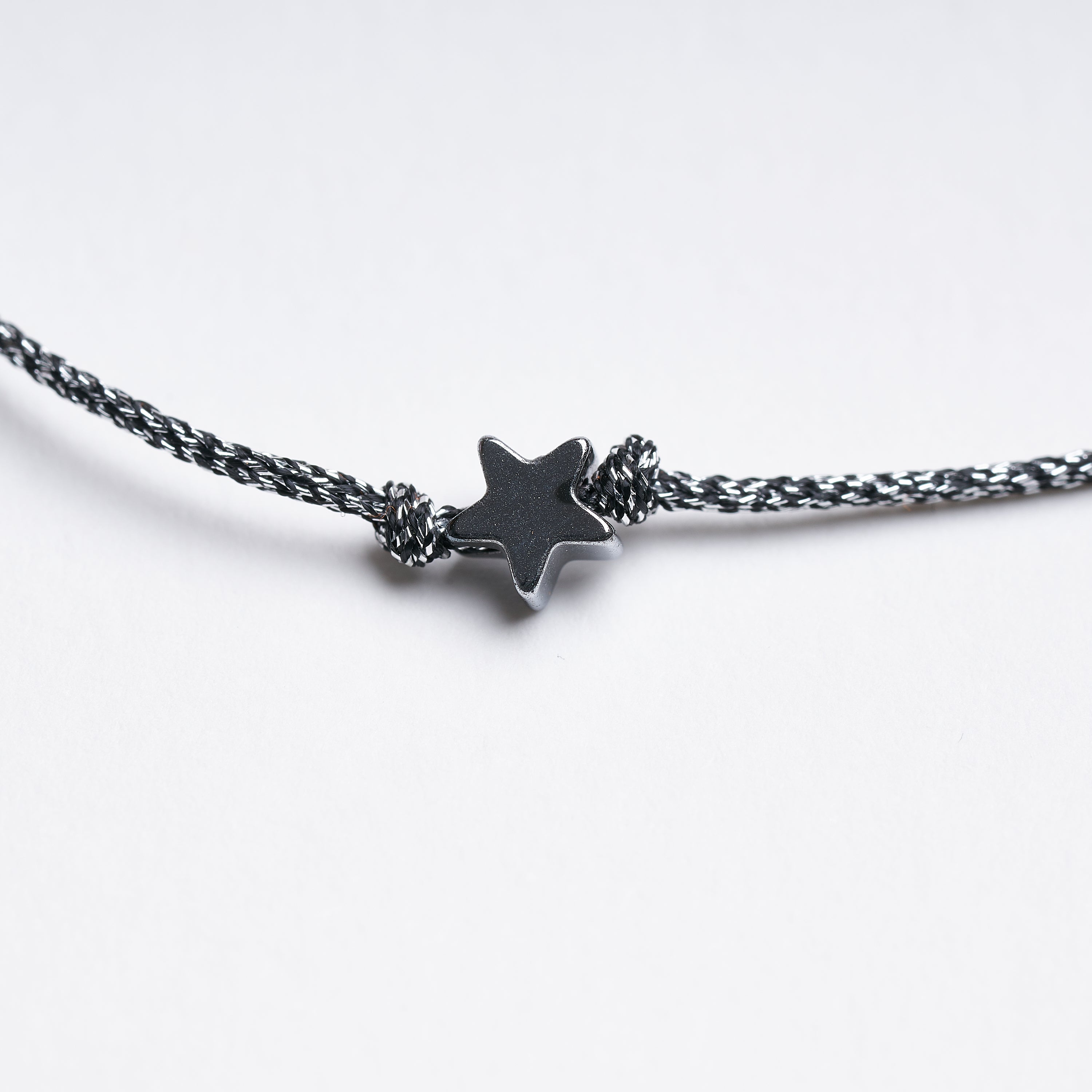 Pulsera con estrella diminuta de hematita sobre fondo blanco, mostrando su diseño delicado y cordón metálico gris oscuro.