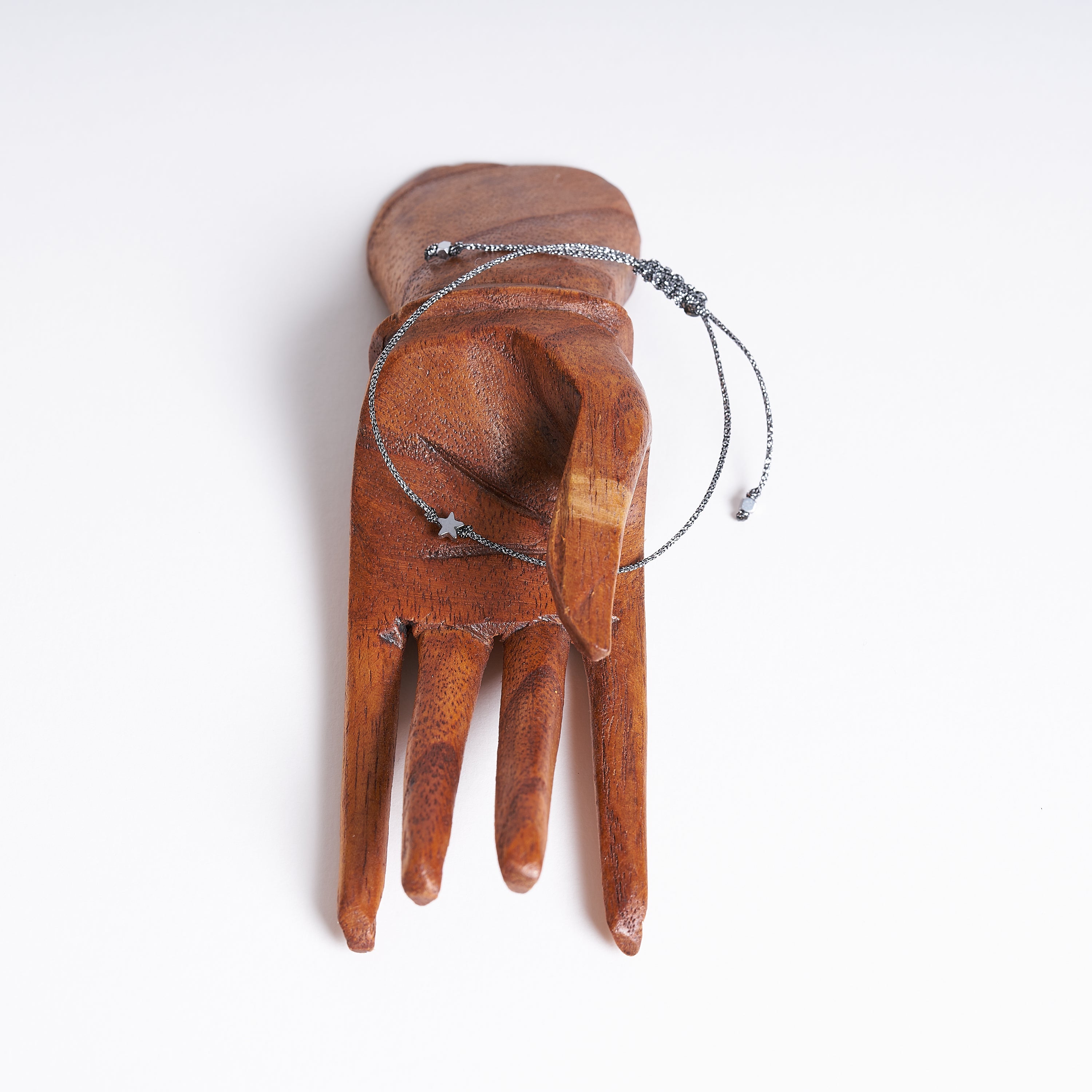 Pulsera con estrella diminuta de hematita sobre fondo blanco, mostrando su diseño delicado y cordón metálico gris oscuro.