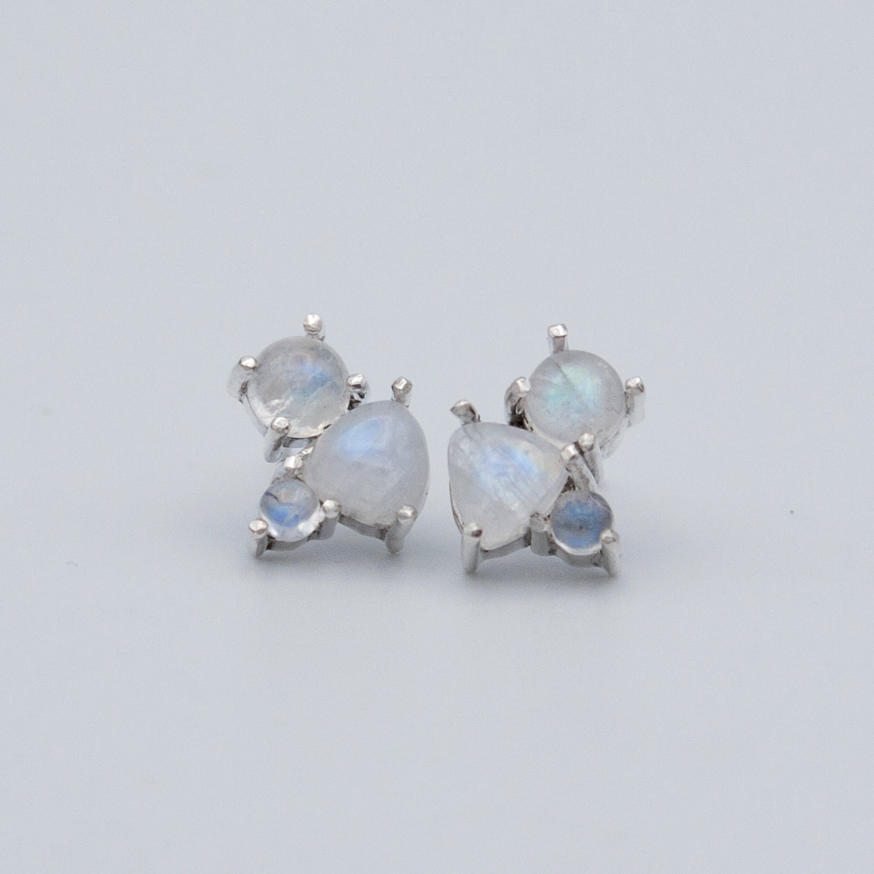 A pair of elegant Rainbow Moonstone Cluster Sterling Silver Earrings featuring round and trillion cut gemstones set in .925 sterling silver.