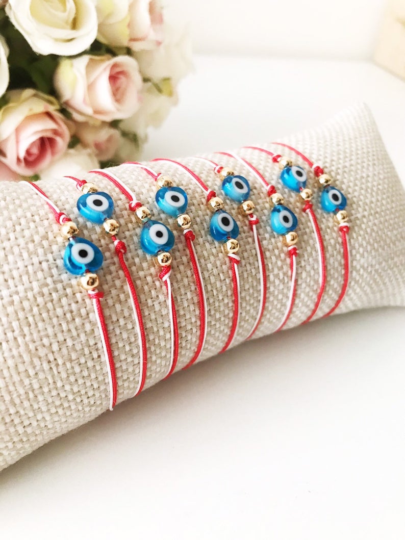 A handmade Red Evil Eye Bracelet featuring a turquoise evil eye bead on a red and white adjustable string, symbolizing protection and good luck.
