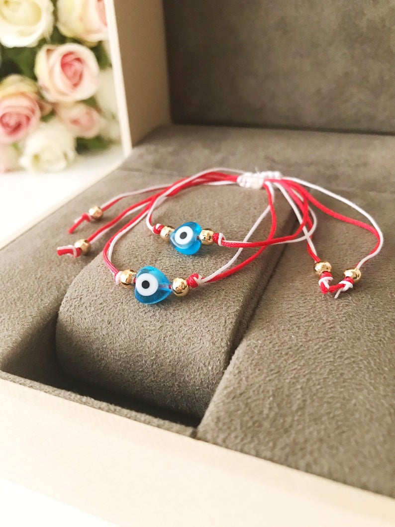 A handmade Red Evil Eye Bracelet featuring a turquoise evil eye bead on a red and white adjustable string, symbolizing protection and good luck.