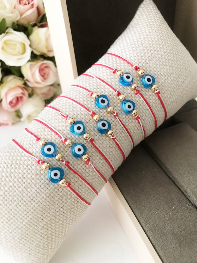 A handmade Red Evil Eye Bracelet featuring a turquoise evil eye bead on a red and white adjustable string, symbolizing protection and good luck.