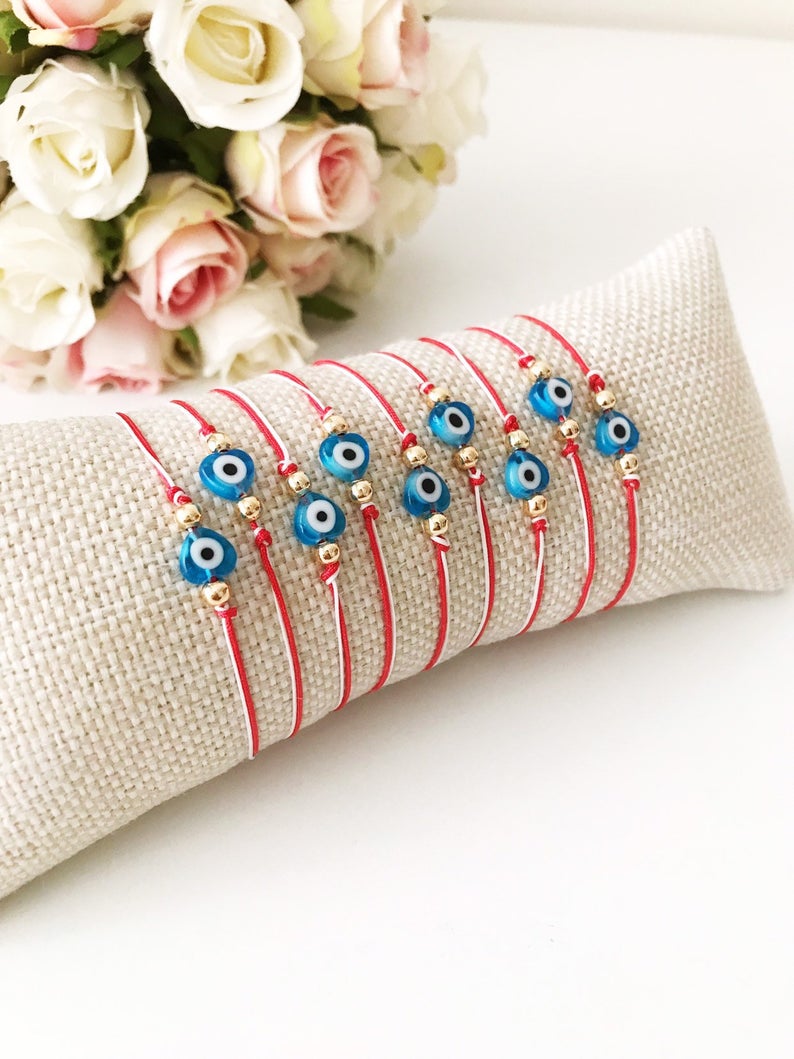 A handmade Red Evil Eye Bracelet featuring a turquoise evil eye bead on a red and white adjustable string, symbolizing protection and good luck.