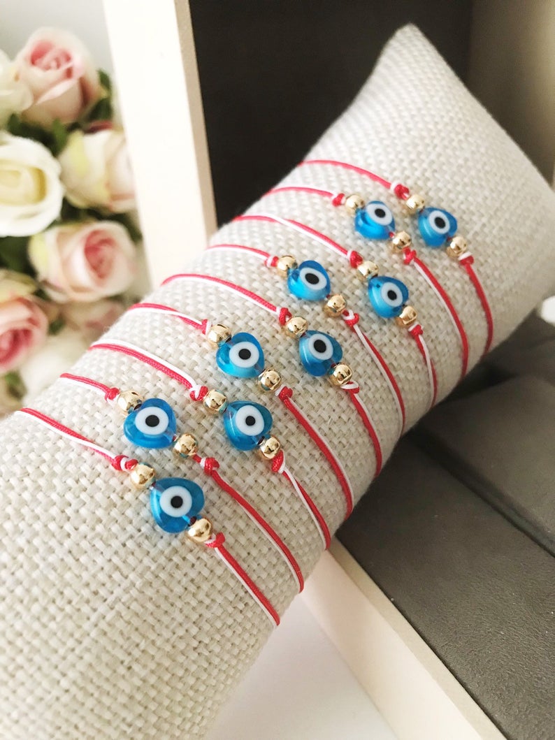 A handmade Red Evil Eye Bracelet featuring a turquoise evil eye bead on a red and white adjustable string, symbolizing protection and good luck.