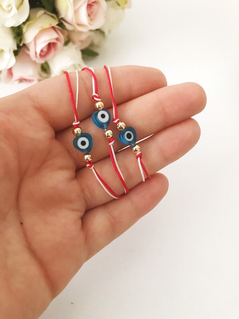 A handmade Red Evil Eye Bracelet featuring a turquoise evil eye bead on a red and white adjustable string, symbolizing protection and good luck.