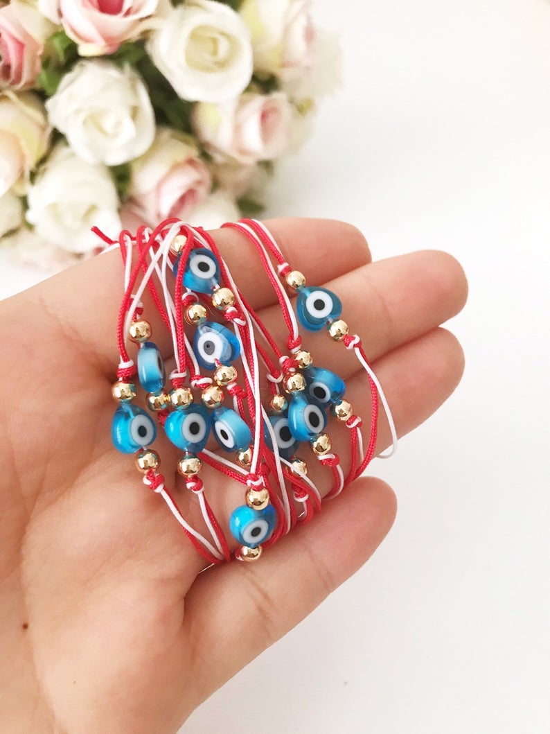 A handmade Red Evil Eye Bracelet featuring a turquoise evil eye bead on a red and white adjustable string, symbolizing protection and good luck.
