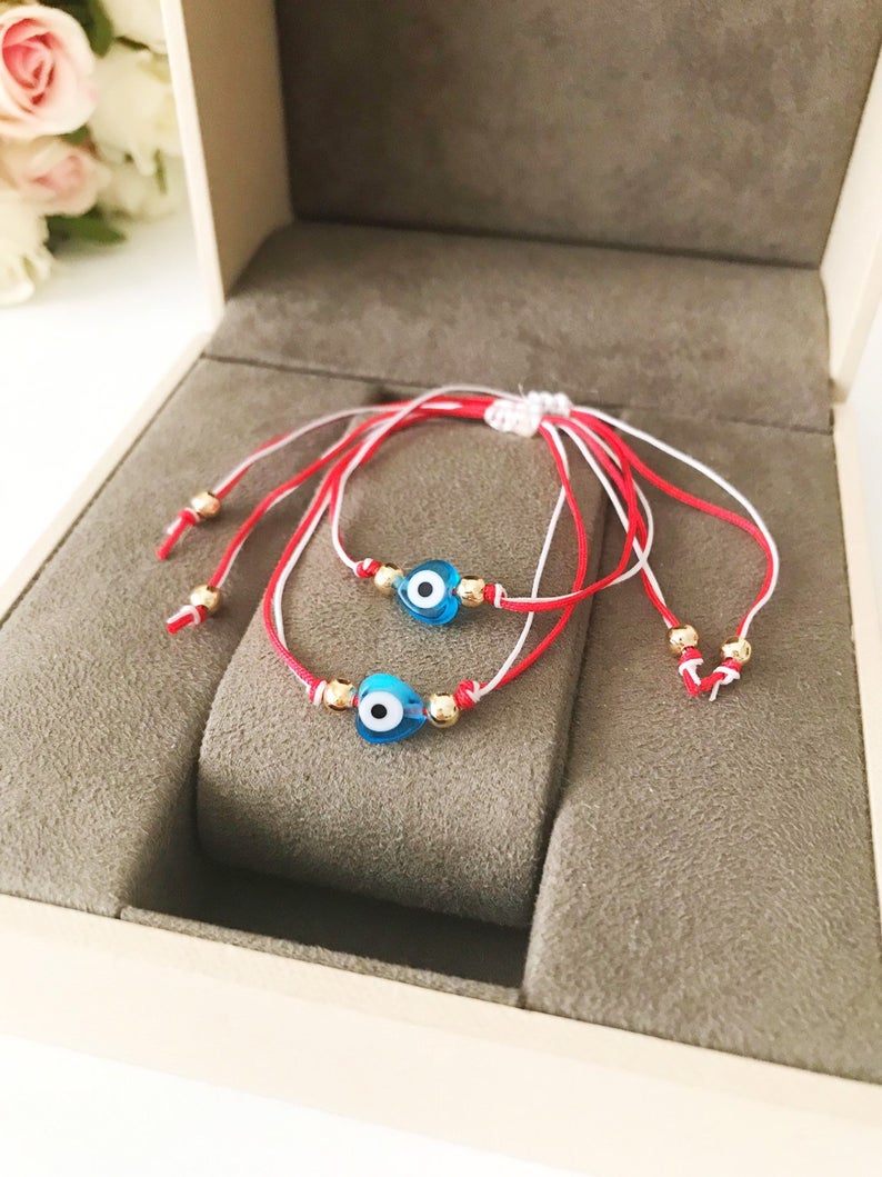 A handmade Red Evil Eye Bracelet featuring a turquoise evil eye bead on a red and white adjustable string, symbolizing protection and good luck.