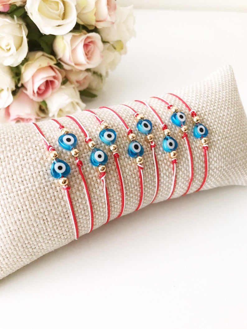 A handmade Red Evil Eye Bracelet featuring a turquoise evil eye bead on a red and white adjustable string, symbolizing protection and good luck.
