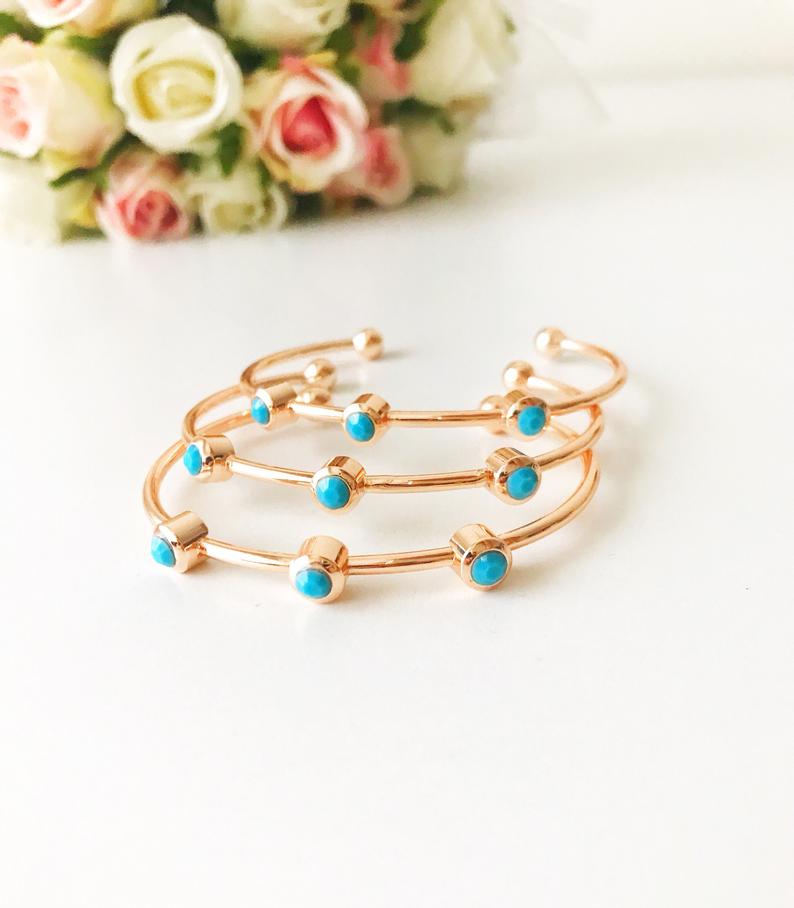 A beautiful rose gold bangle bracelet featuring turquoise beads and a movable oval evil eye charm, showcasing its elegant design.