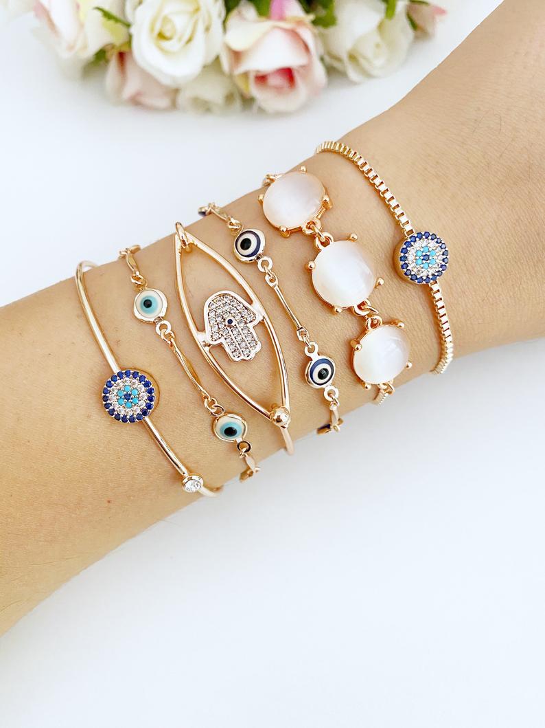 A beautiful rose gold bracelet set featuring an evil eye charm and hamsa hand design, showcasing intricate details and an adjustable fit.