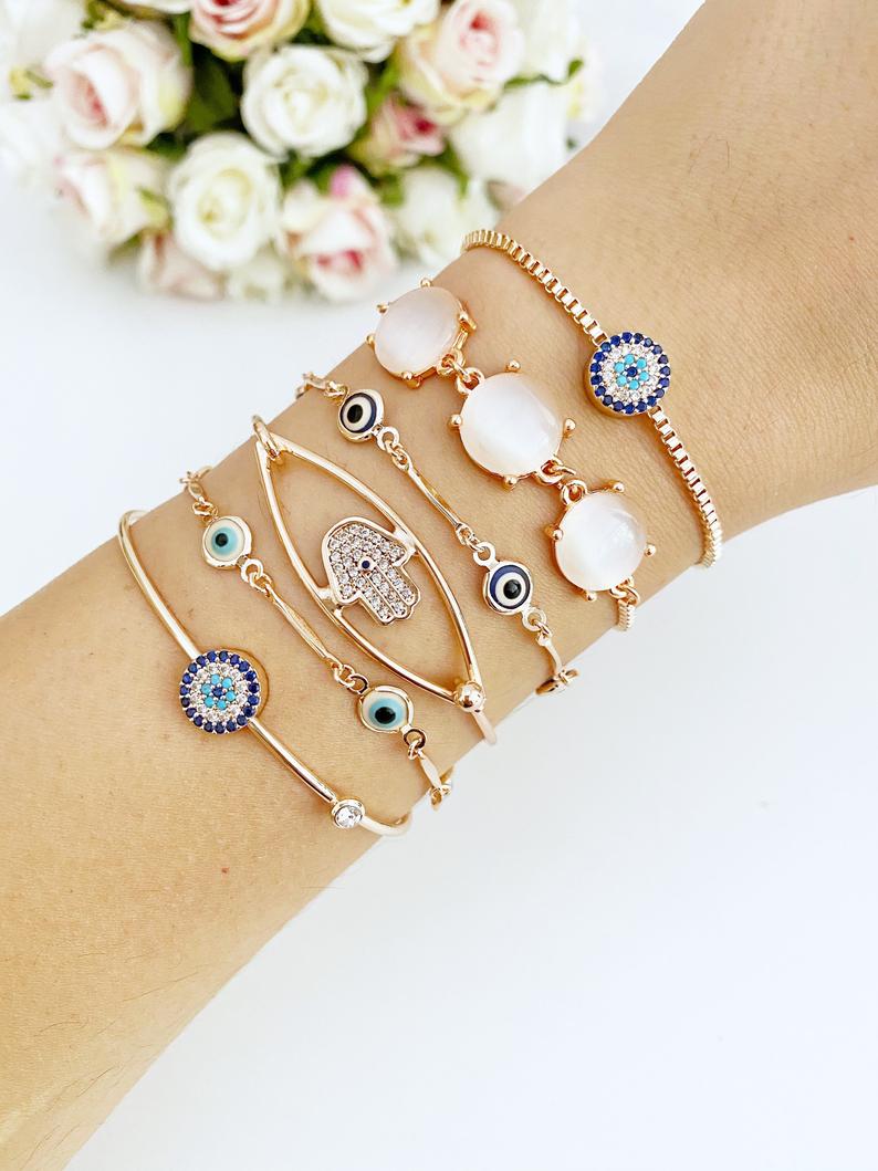 A beautiful rose gold bracelet set featuring an evil eye charm and hamsa hand design, showcasing intricate details and an adjustable fit.