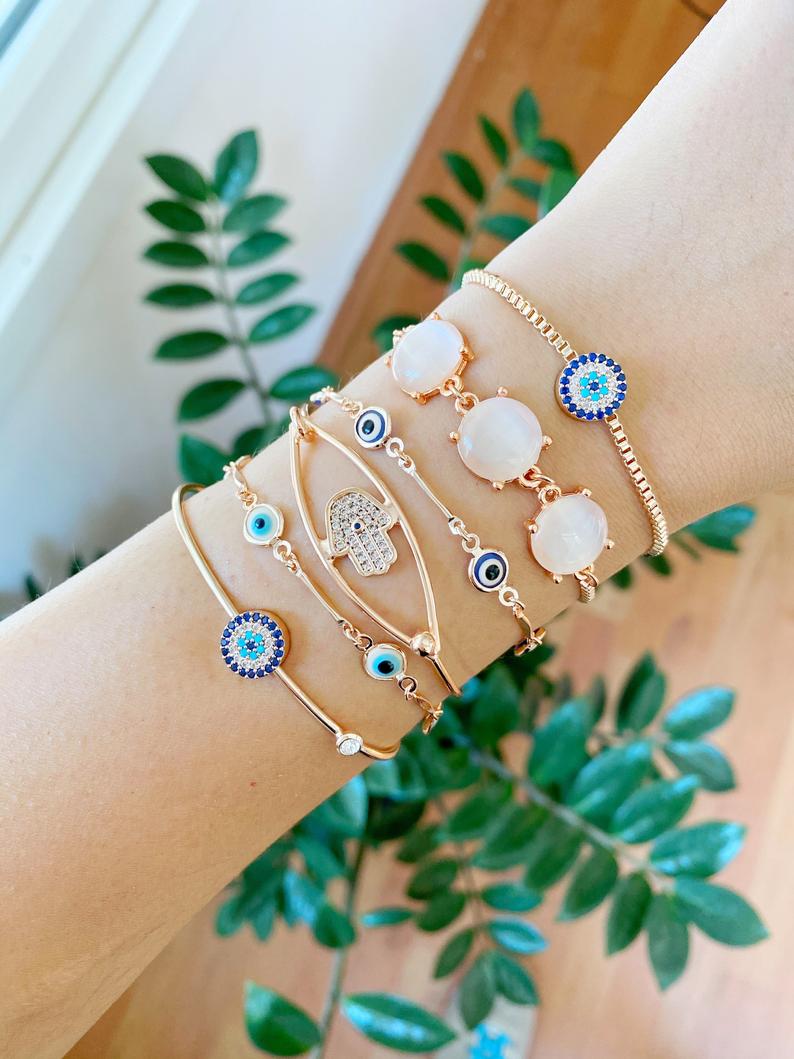 A beautiful rose gold bracelet set featuring an evil eye charm and hamsa hand design, showcasing intricate details and an adjustable fit.
