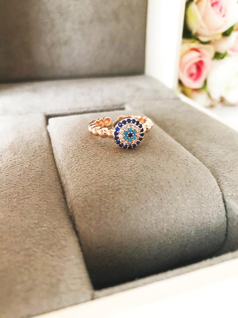 A beautiful rose gold evil eye ring featuring a blue evil eye and sparkling cubic zirconia accents, adjustable for a perfect fit.