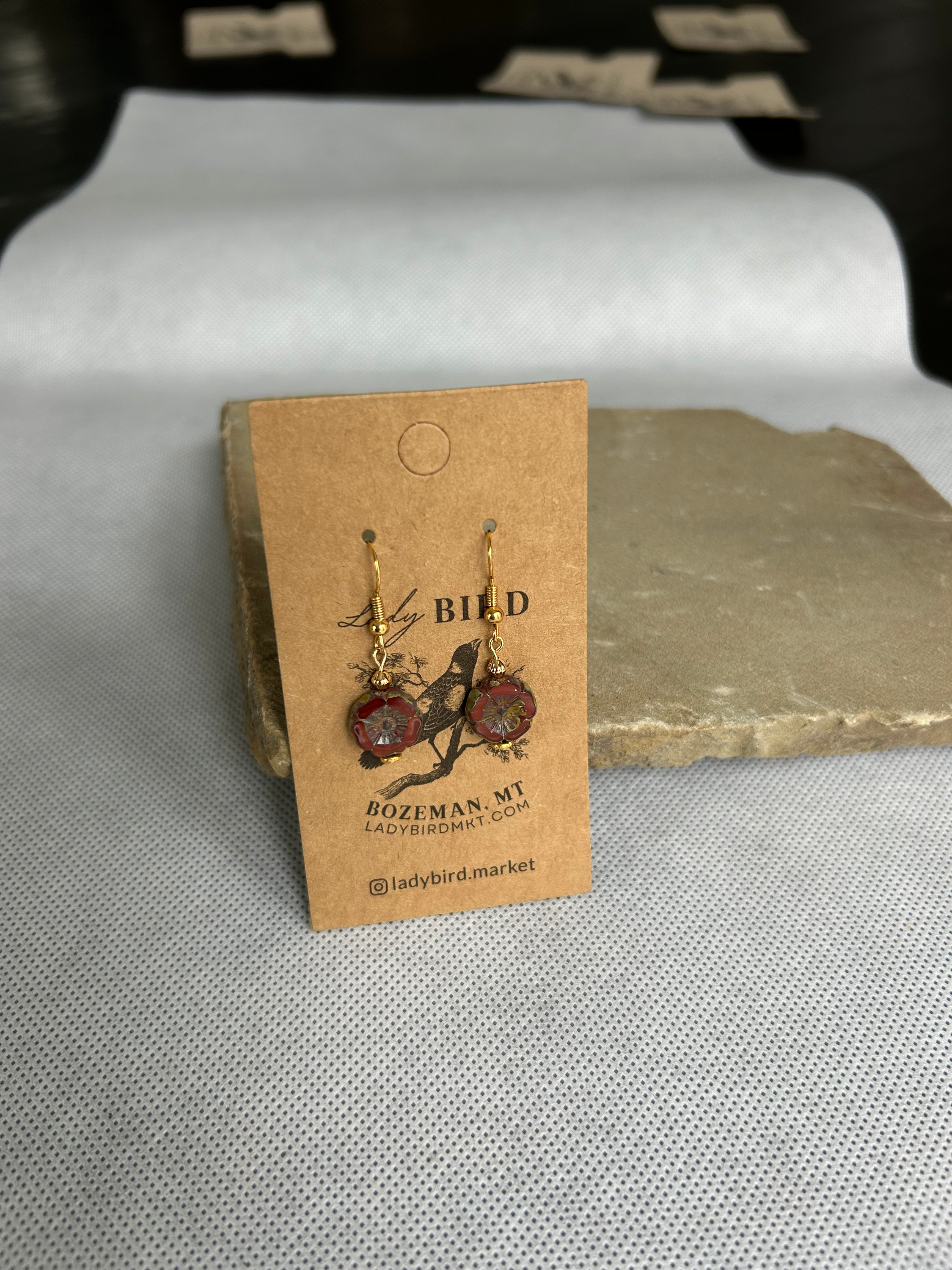 Rustic red etched glass hibiscus flower coin earrings, showcasing vibrant burgundy color and intricate wild rose design.