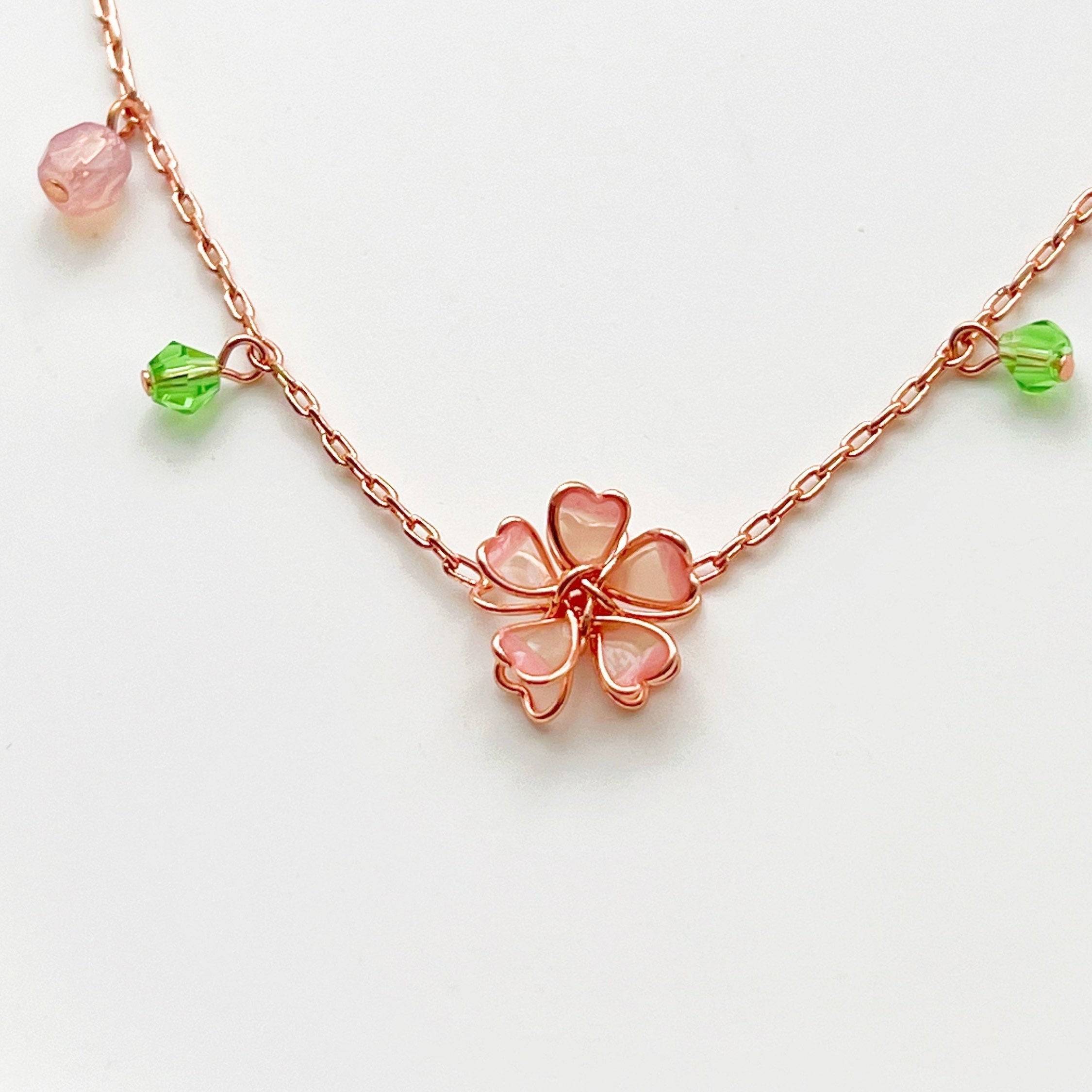 Sakura Flower Necklace featuring pink cherry blossoms and green crystal, handmade with rose gold wire.